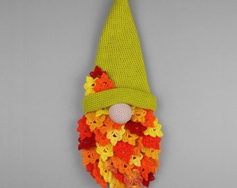 May include: A crocheted gnome ornament with a green hat and a beard made of colourful crocheted leaves. The gnome is hanging from a string.