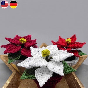 以下が含まれることがあります： 鉢植えの編みぐるみポインセチアが3つ。1つは白、2つは赤です。