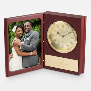 May include: A wooden clock and picture frame combination. The clock has a gold-colored face with Roman numerals and the text "DANBURY Quartz". The picture frame holds a photo of a couple. A gold plaque below the clock has engraved text.