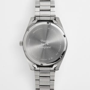 Puede incluir: Un reloj de acero inoxidable con una correa plateada. La esfera del reloj tiene el texto "Thank You & Congrats!". El reloj es de Citizen Watch Co. y es resistente al agua hasta 10 bar.