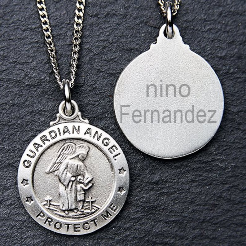 Puede incluir: Collar de plata con colgante de &aacute;ngel de la guarda con una cadena de plata. El colgante presenta una representaci&oacute;n de un &aacute;ngel de la guarda con las palabras "Guardian Angel Protect Me" alrededor del borde. El collar tambi&eacute;n incluye una etiqueta de plata separada con el nombre "nino Fernandez" grabado en ella.