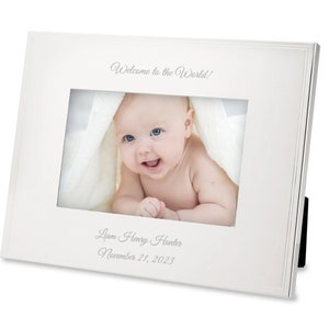 May include: White picture frame with a silver border and a baby photo inside. The frame has the text "Welcome to the World!" at the top and "Liam Henry Hunter November 21, 2023" at the bottom.