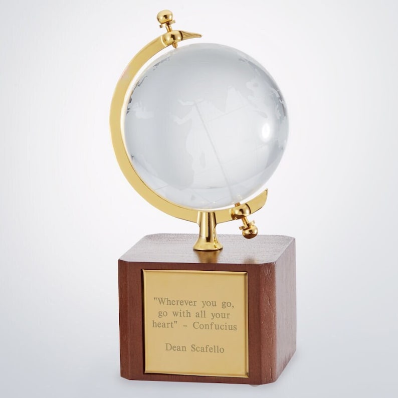 May include: A small, clear glass globe on a gold stand with a wooden base. The base has a gold plaque with the quote "Wherever you go, go with all your heart" - Confucius and the name Dean Scafello.