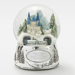 May include: A silver musical snow globe with a winter scene inside. The scene features a white castle with blue towers, a train traveling through a tunnel, and snow-covered trees. The base of the snow globe has a silver oval with the text "May the magic of Christmas fill your home & heart The Englands".