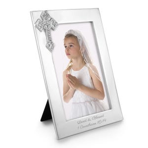 May include: Silver-toned picture frame with a cross design and a white mat. The frame has a stand and a quote that reads "Loved & Blessed 1 Corinthians 16:14".