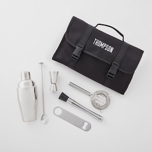 May include: A black canvas bar tool kit with the name "THOMPSON" in white lettering. The kit includes a cocktail shaker, bar spoon, jigger, muddler, strainer, and bottle opener. The tools are silver-colored.