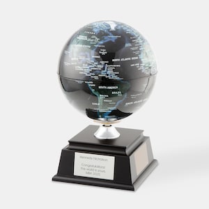 May include: A black and silver globe on a black base. The globe features a detailed map with country names. The base has a silver plaque with text that reads "Kennedy Nicholson Congratulations! The world is yours. MBA 2025."