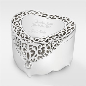 May include: A heart-shaped silver keepsake box with a filigree metal lid and a small pearl accent at the front. The center of the lid is engraved with the text: Grandma Lurlie you're the best! Love, Parker. The box features a smooth finish.