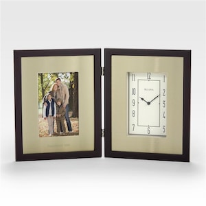 May include: A hinged, dark brown wooden frame with a gold-colored interior. One side holds a family photo, the other a clock with the brand name "Bulova". The clock has a white face with black numerals and hands. The photo frame has the text "Established 2004".