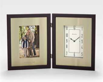 May include: A hinged, dark brown wooden frame with a gold-colored interior. One side holds a family photo, the other a clock with the brand name "Bulova". The clock has a white face with black numerals and hands. The photo frame has the text "Established 2004".
