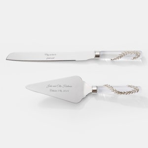 May include: A silver cake knife and server set with clear handles decorated with silver leaf designs. The knife is engraved with the text "May our love be forever sweet". The server is engraved with the text "Jake and Ella Hartman October 17th, 2024".