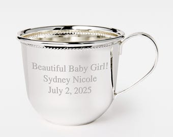 May include: A silver baby cup with a handle, featuring the engraved text "Beautiful Baby Girl! Sydney Nicole July 2, 2025." The cup has a beaded rim and a polished finish, perfect for a baby shower gift.