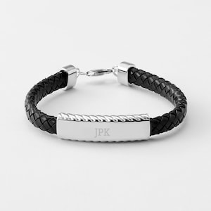 May include: A black leather bracelet with a silver clasp and a silver rectangular tag engraved with the initials "JPK".