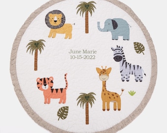 May include: A white round baby play mat with a brown border and a variety of animal illustrations, including a lion, elephant, zebra, giraffe, and tiger. The mat also features palm trees and the text "June Marie 10-15-2022".