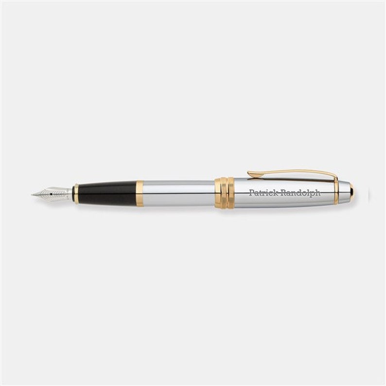 May include: A silver and gold fountain pen with a black ink cartridge. The pen is engraved with the name "Patrick Randolph".
