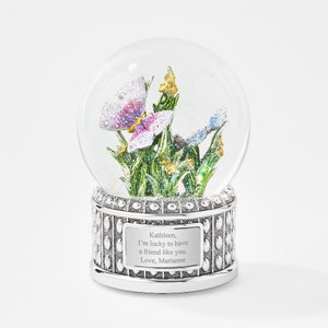 May include: A silver snow globe with a butterfly and flowers inside. The base has a personalized message that reads "Kathleen, I'm lucky to have a friend like you. Love, Marianne".