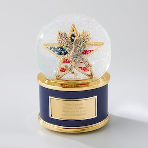 May include: A blue snow globe with a gold base and a gold star with an American flag and a golden eagle. The base has a gold plaque with the text "Vicky Gonzalez 20 Years US Army Thank you for your service and sacrifice."