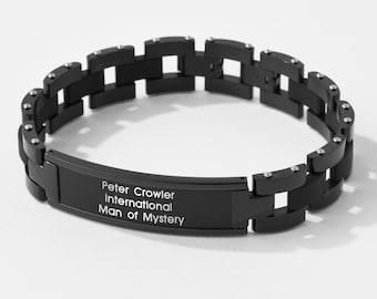 May include: Black bracelet with a silver-toned clasp and a black plate engraved with the text "Peter Crowler International Man of Mystery".