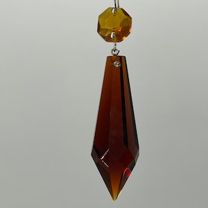 May include: A brown crystal teardrop pendant with a smaller amber crystal octagon at the top.