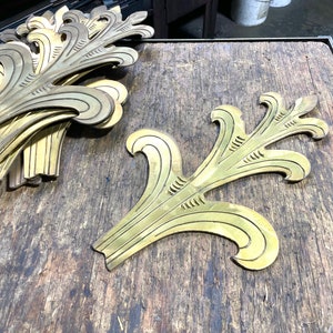 May include: A stack of gold-colored metal leaf-shaped decorative pieces on a wooden surface. One piece is laying flat on the surface.