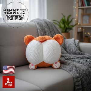 Puede incluir: Un cojín de crochet naranja y blanco con forma de trasero de corgi con almohadillas rosas. El cojín está sobre un sofá gris con una manta gris. La imagen incluye el texto "CROCHET PATTERN" en un diseño circular.