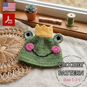 May include: A green crochet frog hat with a yellow crown, pink cheeks, and black eyes. The hat is designed for children aged 1-3 years. The image also includes the text "CROCHET PATTERN" and "Size: 1-3 y."