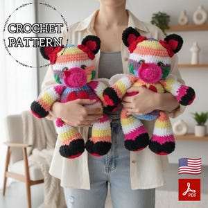 May include: Two handmade crochet cow plushies. Each cow has a rainbow striped body, black hooves, and black and red ears. The cows have pink noses and red hearts. The text "CROCHET PATTERN" is in a circle above the plushies.