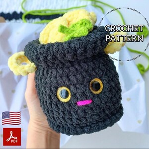 May include: A crocheted black cauldron with yellow and green accents, featuring large golden eyes and a pink stitched mouth. The cauldron holds a yellow and green crocheted vegetable. The text "CROCHET PATTERN" is visible.