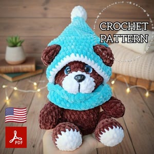 Könnte beinhalten: Ein handgefertigter brauner Teddybär mit hellblauer Mütze und Schal mit weißer Bordüre. Der Bär hat blaue Augen und eine weiße Schnauze. Der Text "CROCHET PATTERN" und ein PDF-Symbol mit der amerikanischen Flagge sind enthalten.