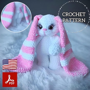 Pode incluir: Um coelho de crochê branco e rosa. O coelho tem orelhas longas e listradas em rosa e branco. Os olhos são detalhados. A imagem inclui o texto "CROCHET PATTERN" e um ícone PDF.