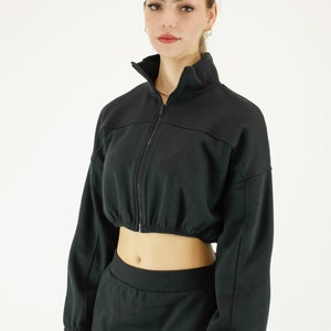 May include: A black cropped zip-up jacket with long sleeves and a matching black skirt with a red and blue stripe down the side.