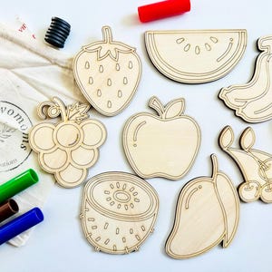K&ouml;nnte beinhalten: Ein Set aus acht unfertigen Holzfr&uuml;chten zum Bemalen oder Dekorieren. Die Formen umfassen eine Erdbeere, Trauben, einen Apfel, eine Wassermelone, eine Kiwi, eine Mango, eine Banane und Kirschen.