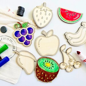K&ouml;nnte beinhalten: Ein Set aus Holzfr&uuml;chten zum Ausmalen, darunter eine Erdbeere, eine Wassermelone, ein Apfel, Trauben, eine Banane, eine Mango, eine Kiwi und Kirschen. Die Formen sind unvollendet und bereit, mit Markern oder Buntstiften ausgemalt zu werden. Das Set enth&auml;lt auch Marker und eine Tasche zur Aufbewahrung.