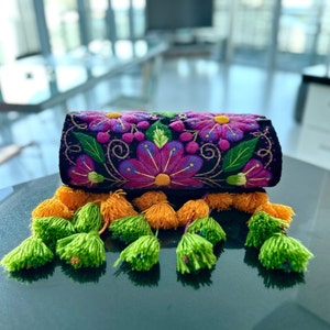 May include: A black embroidered clutch bag with colorful floral designs and green and yellow tassels.