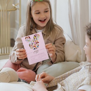 May include: Pink invitation with a Mickey Mouse head made of Disney characters. The invitation says "Join us for a Magical Celebration, Lia's 1th Birthday, Saturday, Dec 11th, 2:00 PM - 4:00 PM, 210N Westwood, Los Angeles, CA, RSVP Rinaldo 555-202-386".