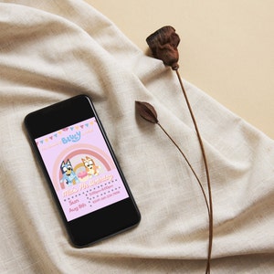 May include: A smartphone displaying a digital invitation for a 7th birthday party. The invitation features the characters Bluey and Bingo from the animated television show Bluey. The invitation is pink and features a rainbow. The text on the invitation reads "Have a 7th Birthday" and includes the date, time, and RSVP information.