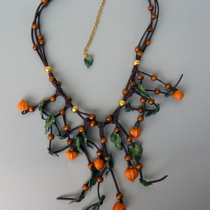 Peut inclure: Un collier en cuir marron avec des perles dorées et des accents orange et vert. Le collier présente un groupe de petits charmes orange et vert qui ressemblent à des feuilles et des fleurs.