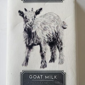 May include: A rectangular bar of goat milk soap with a black and white illustration of a goat. The soap is labeled "ALCHIMIA" and "GOAT MILK", with text indicating it is fine vegetable soap, handmade in Italy, and weighs 10.5 oz.