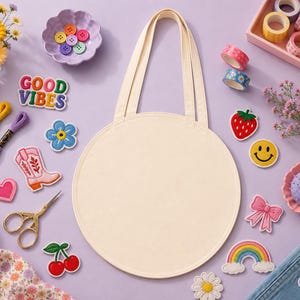 Puede incluir: Un bolso tote de color crema con asas largas, rodeado de materiales de manualidades y parches decorativos. Los parches incluyen una fresa, una carita sonriente, un arcoíris y las palabras "Good Vibes". Otros artículos incluyen hilo de bordar, cinta washi y un pequeño ramo de flores.