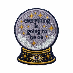May include: A circular embroidered patch shaped like a crystal ball with a dark blue border. The center features the text everything is going to be ok in dark blue letters, surrounded by yellow stars, white clouds, and a central eye motif.