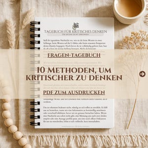 Op de afbeelding: Een spiraalgebonden notitieboek met witte pagina's met de Duitse tekst TAGEBUCH FÜR KRITISCHES DENKEN, FRAGEN-TAGEBUCH, 10 METHODEN, UM KRITISCHER ZU DENKEN en PDF ZUM AUSDRUCKEN, weergegeven met gedroogde bloemstengels en houten kralen.
