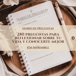 May include: A spiral-bound notebook with the title "DIARIO DE PREGUNTAS" and the text "280 PREGUNTAS PARA REFLEXIONAR SOBRE TU VIDA Y CONOCERTE MEJOR" is open on a wooden tray. A white pen with gold accents rests on the notebook.