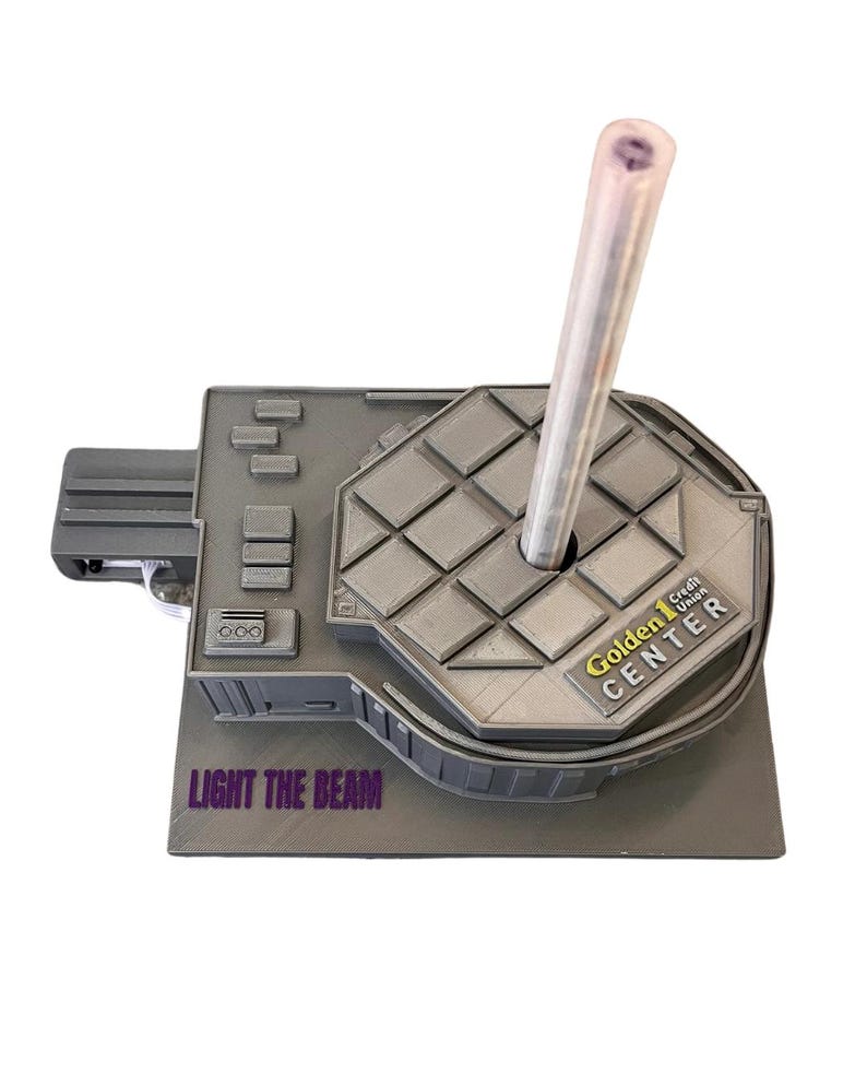 May include: A gray 3D printed model of the Golden 1 Credit Union Center, home of the Sacramento Kings. The model has a clear plastic tube sticking out of the top, and the words "LIGHT THE BEAM" are printed on the base.