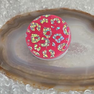 May include: A pink phone grip with a white base and a leopard print design with iridescent glitter.