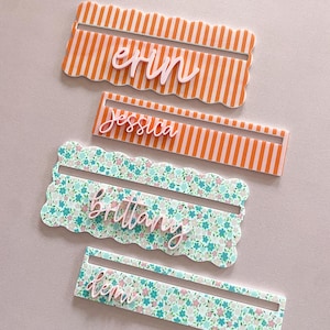 K&ouml;nnte beinhalten: Vier personalisierte Namensschilder. Zwei sind orange und wei&szlig; gestreift mit den Namen "erin" und "jessica". Die anderen beiden sind floral mit den Namen "brittany" und "ken". Jede Karte hat einen gewellten Rand.