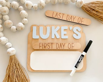 May include: Wooden sign with the text "LUKE'S FIRST DAY OF" and a blank space for writing. The sign is decorated with a light blue nameplate and a white marker is included.