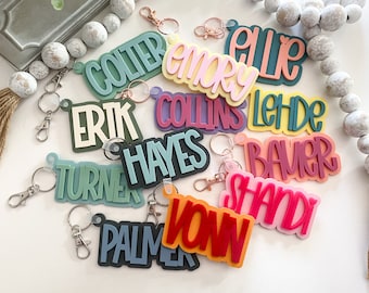 May include: A collection of colorful personalized keychains with names like "Colter", "Emory", "Ellie", "Erik", "Collins", "Leide", "Hayes", "Turner", "Bauer", "Shandy", "Palmer", and "Vown".