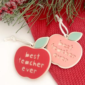 Może przedstawiać: Dwa czerwone ozdoby w kształcie jabłka z napisem "best teacher ever". Ozdoby są wykonane z drewna i mają zielony liść na g&oacute;rze.