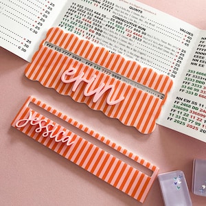 K&ouml;nnte beinhalten: Zwei personalisierte Namensschilder mit den Namen "Erin" und "Jessica" in Schreibschrift. Beide Schilder haben ein rosa-orange gestreiftes Design.