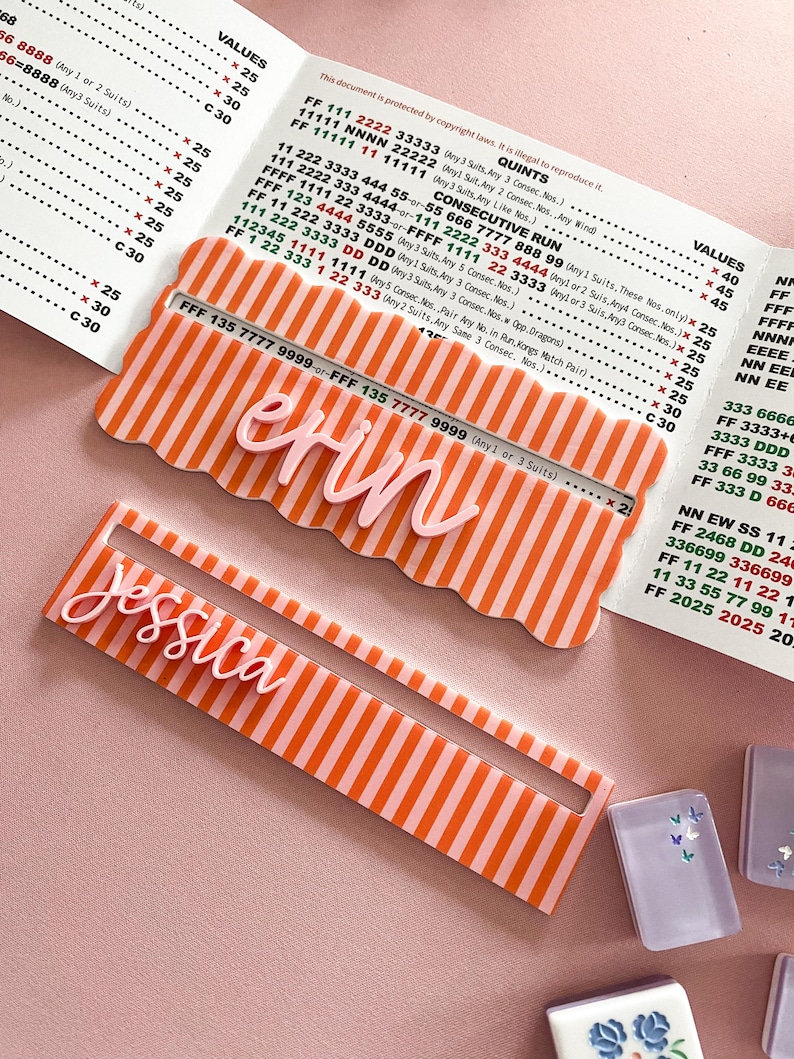 K&ouml;nnte beinhalten: Zwei personalisierte Namensschilder mit den Namen "Erin" und "Jessica" in Schreibschrift. Beide Schilder haben ein rosa-orange gestreiftes Design.